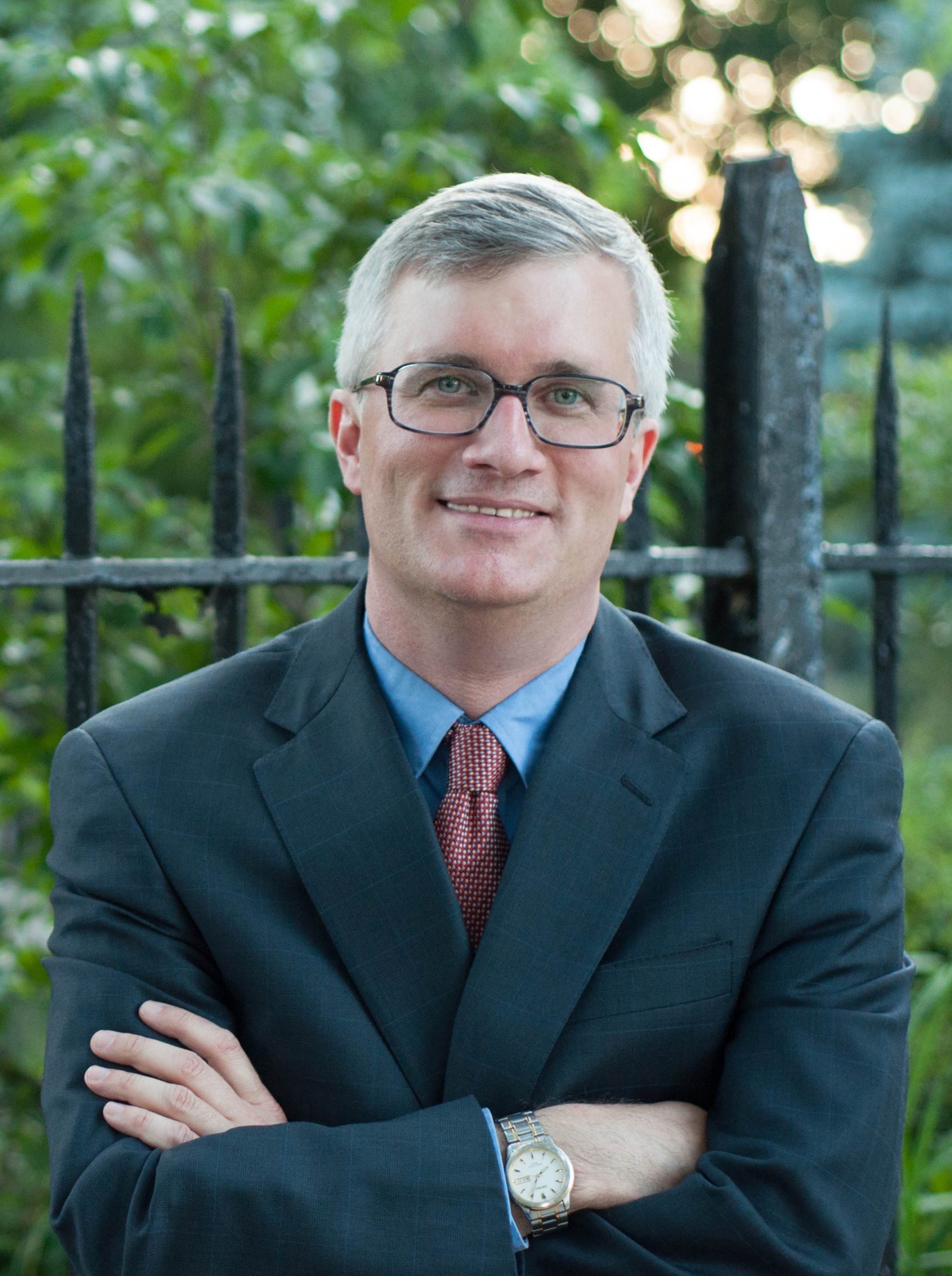 A photo of Senator Kavanagh with his arms crossed in front of a fence.