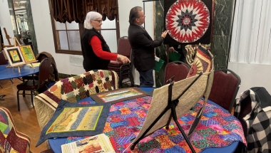 Senator Addabbo admires the handmade quilts by Louise Naples.