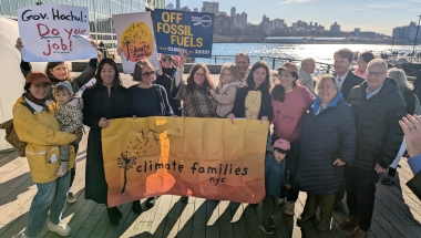 Families and advocates stand with posters supporting the Climate Change Superfund Ac