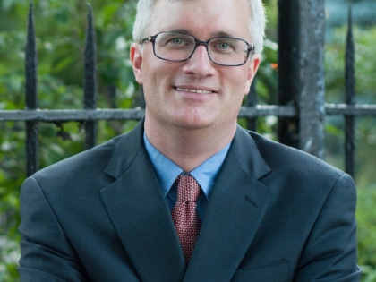 A photo of Senator Kavanagh with his arms crossed in front of a fence.