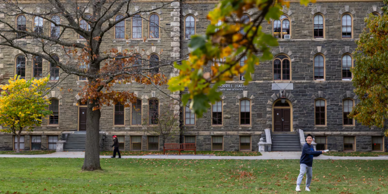 A student throws a frisbee on a field at Cornell University.