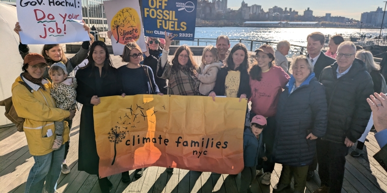 Families and advocates stand with posters supporting the Climate Change Superfund Ac