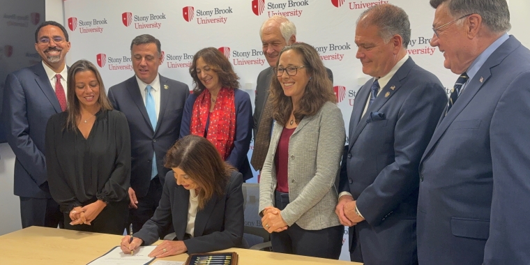 Photo Image of Gov. Kathy Hochul signing a bill sponsored by Sen. Martinez that allows Stony Brook University to develop more on-campus housing. The governor is surrounded by officials including Sen. Martinez during the signing.