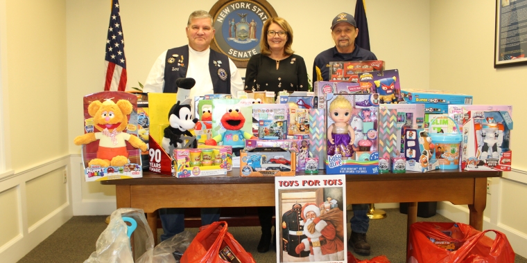 Walworth Lions Club Treasurer Lou Villanova, Senator Pam Helming, and Walworth Lions Club member Dennis Landry stand in Senator Helming’s District Office in Geneva with the toys the Club contributed to her local Toys for Tots drive.